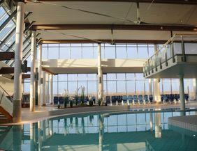 Ein eleganter Innenpool mit großen Fenstern, die viel Tageslicht hereinlassen. Rund um den Pool sind Liegen und Pflanzen für eine entspannende Atmosphäre.