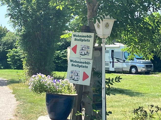 Ein Wohnmobil-Stellplatz mit Schildern und einem geparkten Wohnmobil im Hintergrund.