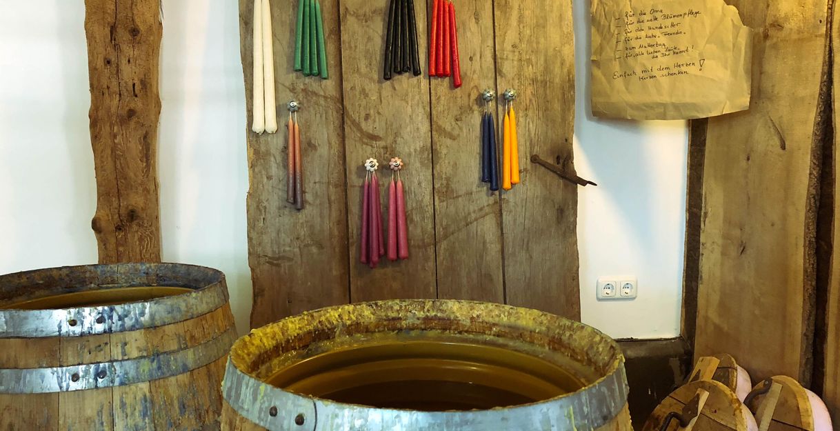 A nostalgic room with old wooden barrels and colorful wax candles on the wall. Notes are attached to a piece of paper.