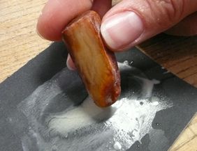 A hand is rubbing a piece of wood on a black sandpaper. There are traces of sanding dust visible.