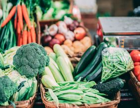 Frisches Gemüse auf einem Wochenmarkt, darunter Brokkoli, Karotten, Zucchini, Tomaten und Bohnen.