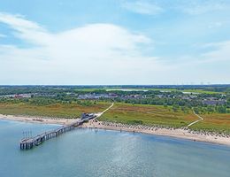 Luftaufnahme des Weissenhäuser Strands mit Steg und Strandkörben, umgeben von grüner Landschaft und Ostsee-Blick.