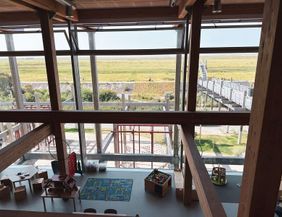 A bright playroom with toys and a carpet. Through large windows, one can see the green landscape outside.