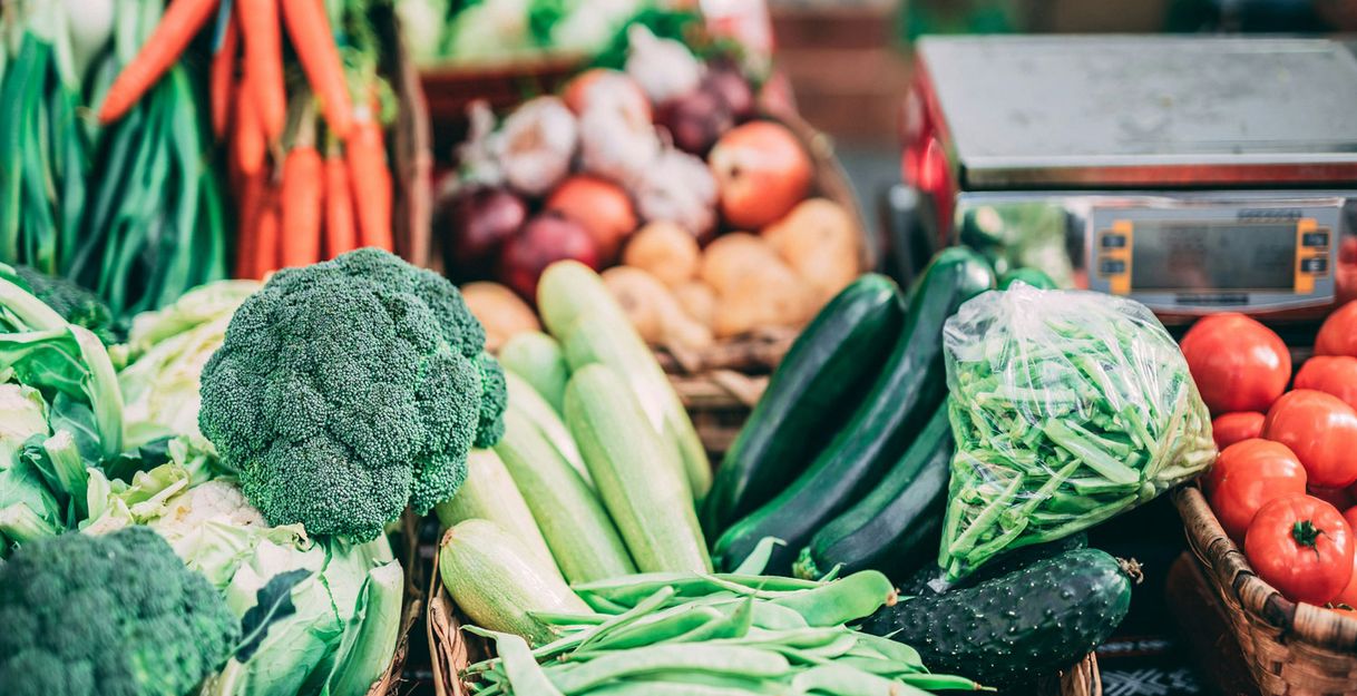 Frisches Gemüse auf einem Wochenmarkt, darunter Brokkoli, Karotten, Zucchini, Tomaten und Bohnen.