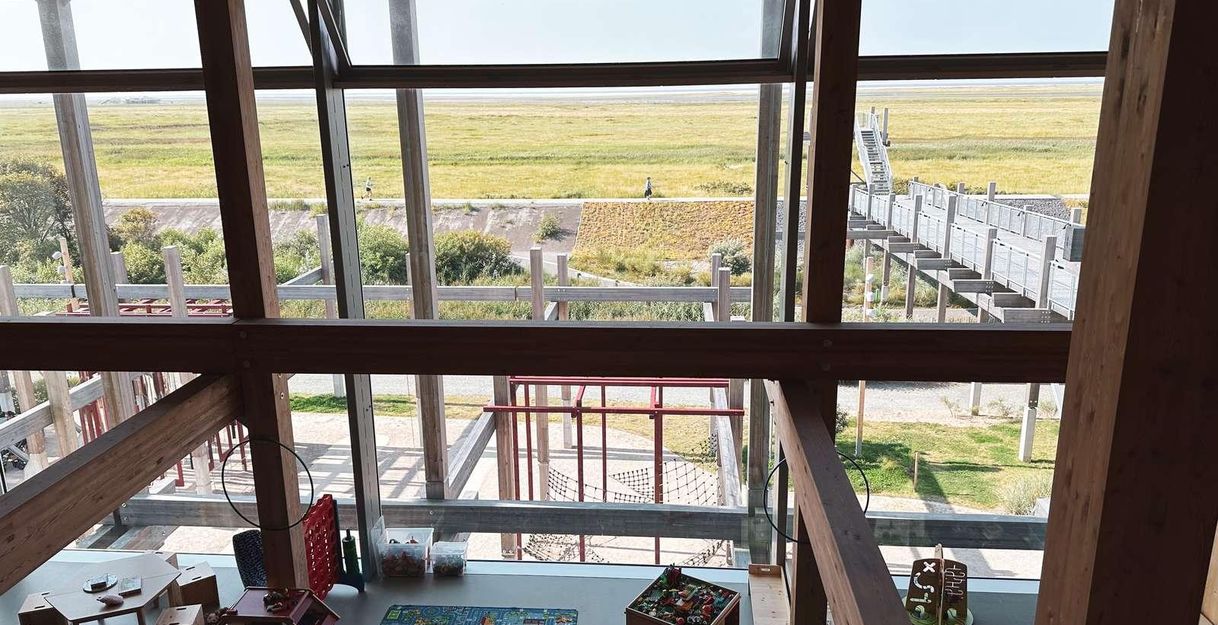 A bright playroom with toys and a carpet. Through large windows, one can see the green landscape outside.