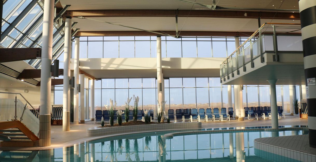 An elegant indoor pool with large windows that let in plenty of natural light. Around the pool, there are loungers and plants for a relaxing atmosphere.