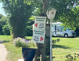 Ein Wohnmobil-Stellplatz mit Schildern und einem geparkten Wohnmobil im Hintergrund.