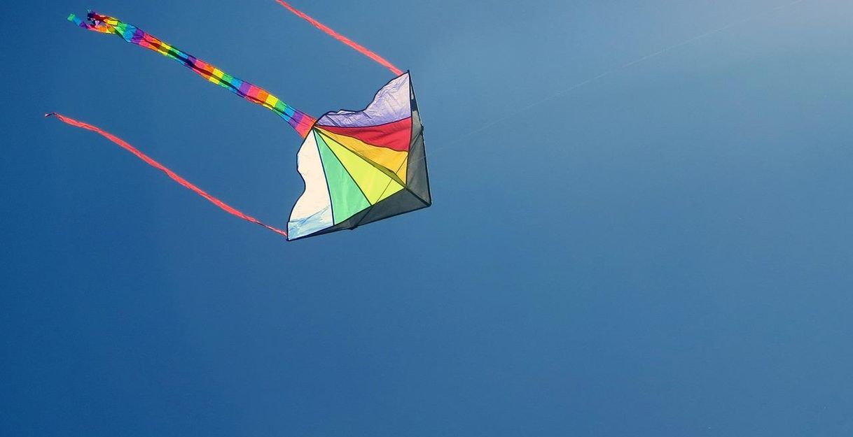 A colorful kite soars high in the clear blue sky. The long, colorful ribbons flutter in the wind.